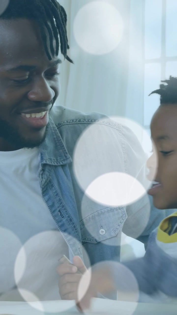 Video verticale: Padre che guida il figlio mentre prende una penna su un blocco al tavolo, per l'apprendimento, con effetto bokeh.
