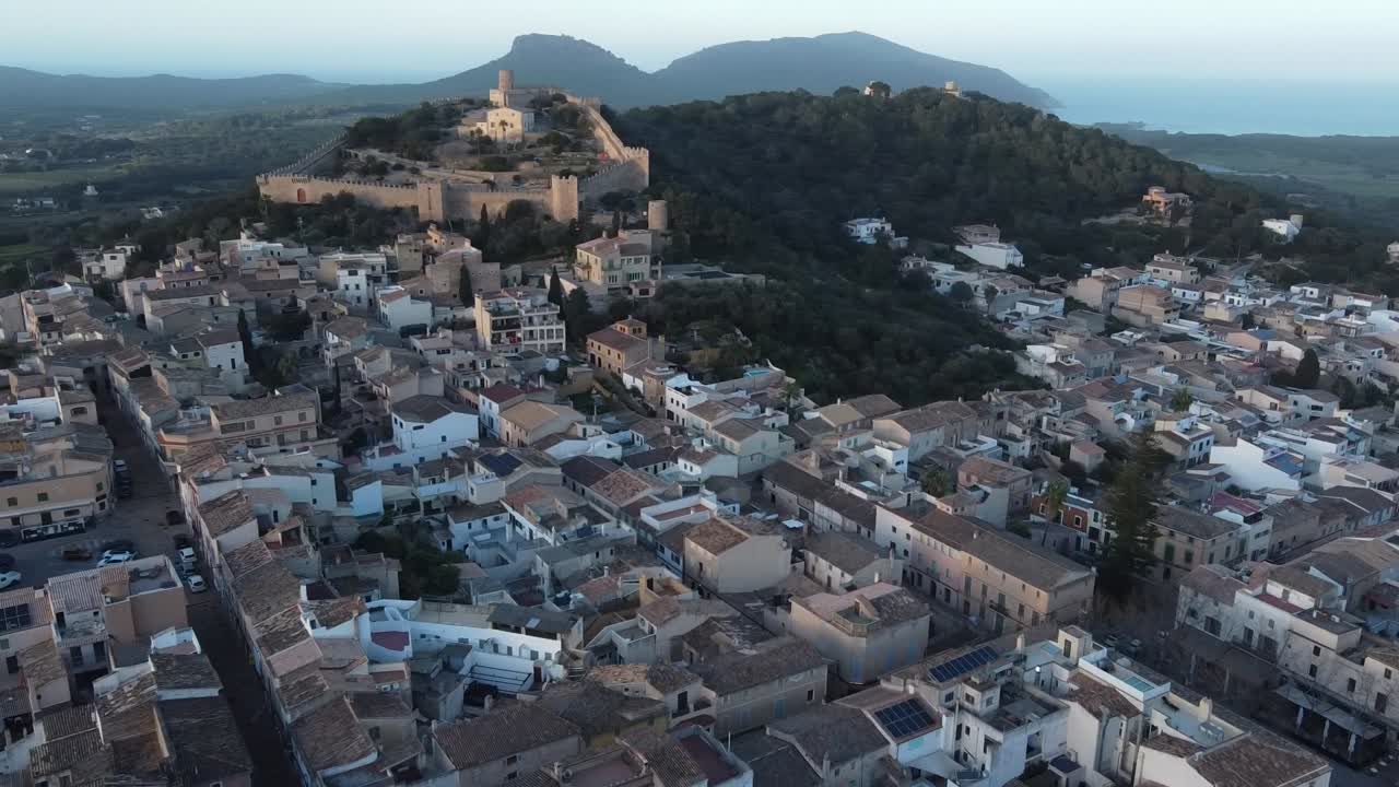 Veduta aerea circolare della città e del castello di Capdepera al tramonto, con Cala Rajada sullo sfondo, Maiorca, Spagna.