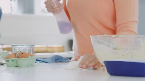 woman cleaning kitchen counter with spray and cloth after cake baking