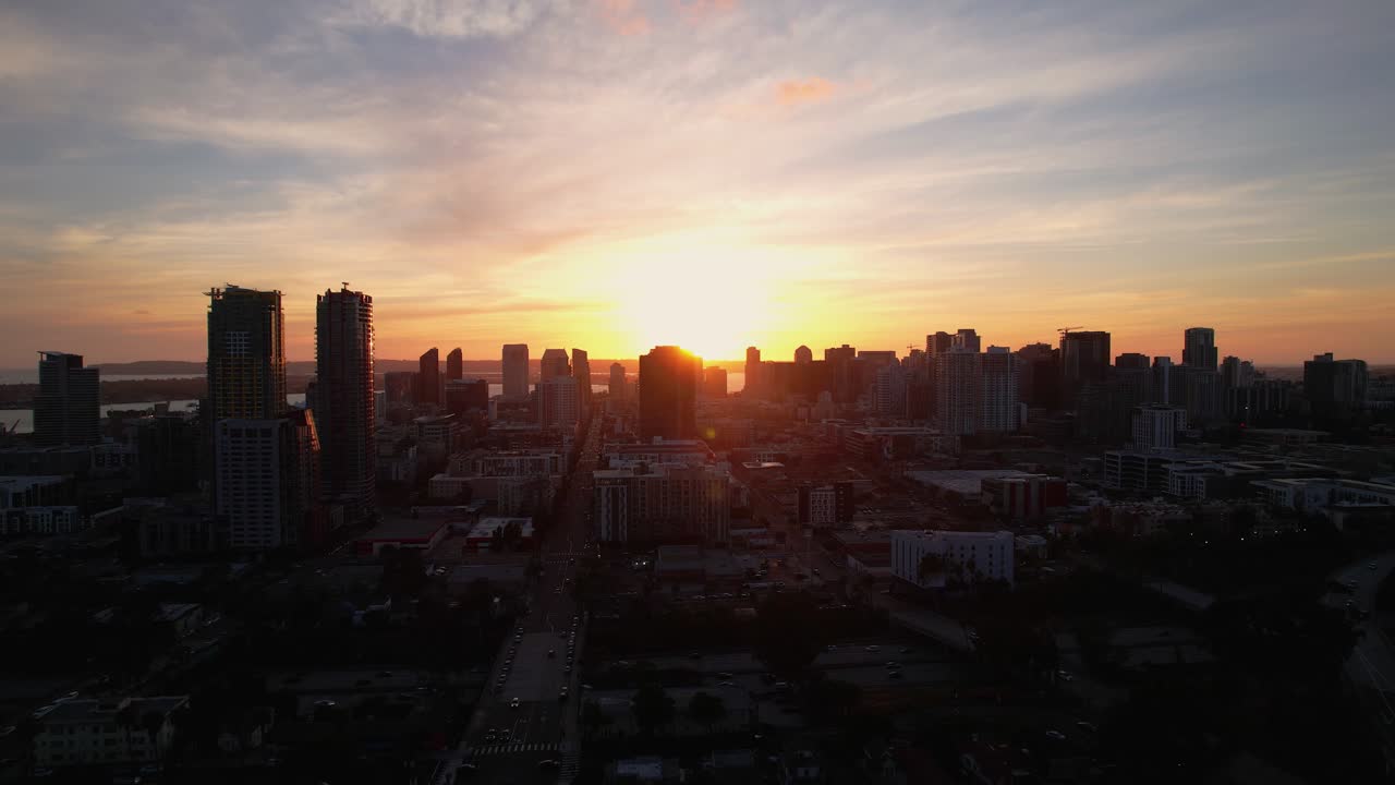 Drone recuando do centro de San Diego às 19h, com a luz do sol refletindo nos edifícios durante a hora dourada