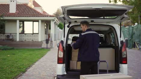 Young-handsome-Caucasian-delivery-man-putting-boxes-in-van-delivering-shipment.-Male-post-office-worker-Courier-concept