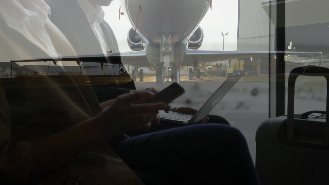 Using laptop and phone, business person working with airplane visible through window