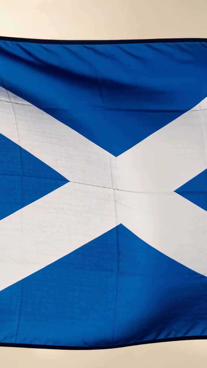 Pystyvideo: Lepattava Saltire-lippu liikkuu tasaisessa tuulessa ulkona, näyttäen ompeleita ja helmaa.