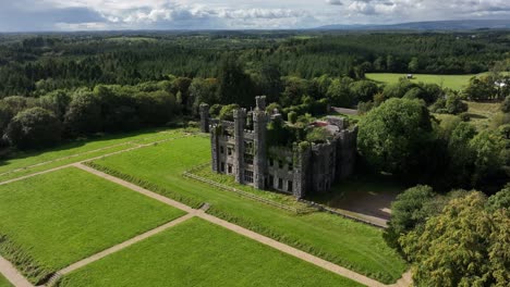 castle saunderson, county cavan, ireland, september 2022. drone orbits counter clockwise and moves closer to ruined stone castle with lawns in front and forrest in background under a cloudy sky.