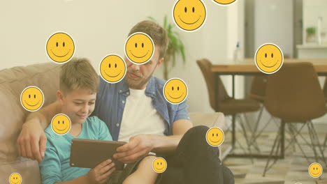 animación de iconos emoji sobre un padre y un hijo caucásicos felices usando una tableta