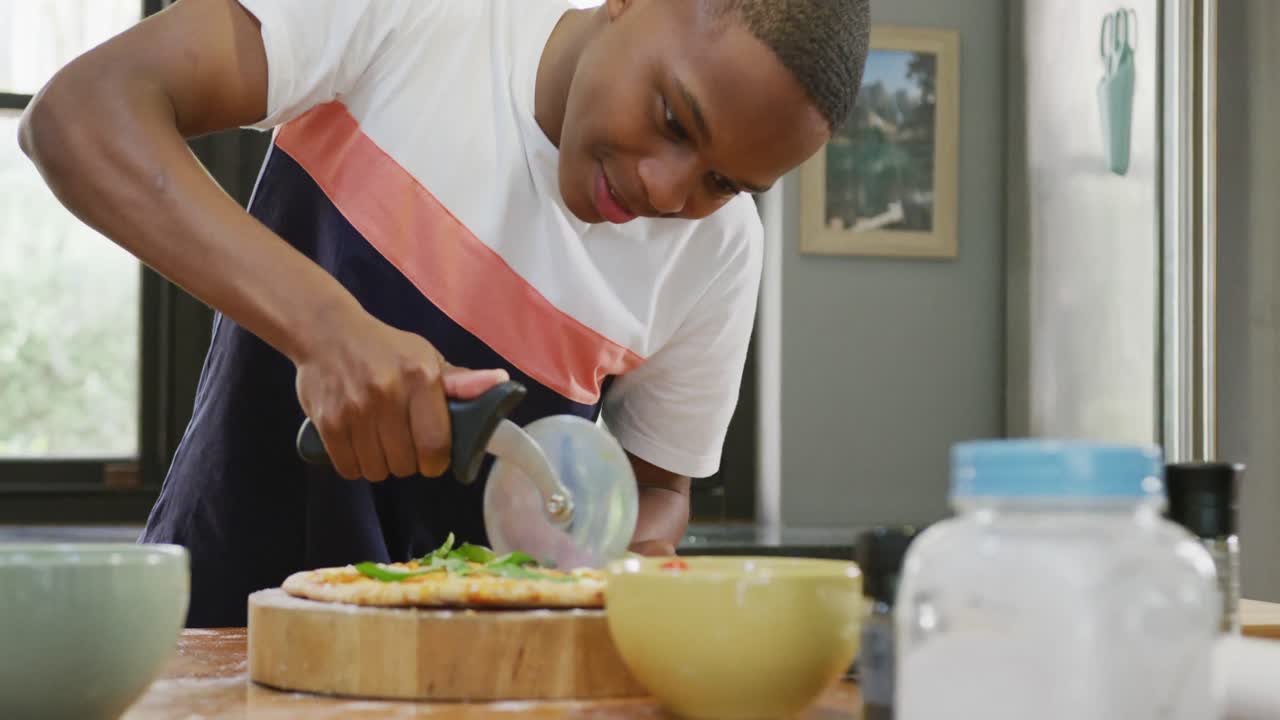 feliz afroamericano varón adolescente cortando pizza en la cocina, cámara lenta