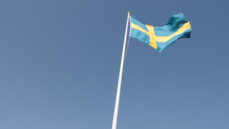 Swedish-flag-on-a-white-pole,-waving-rapidly-in-heavy-wind,-slow-motion