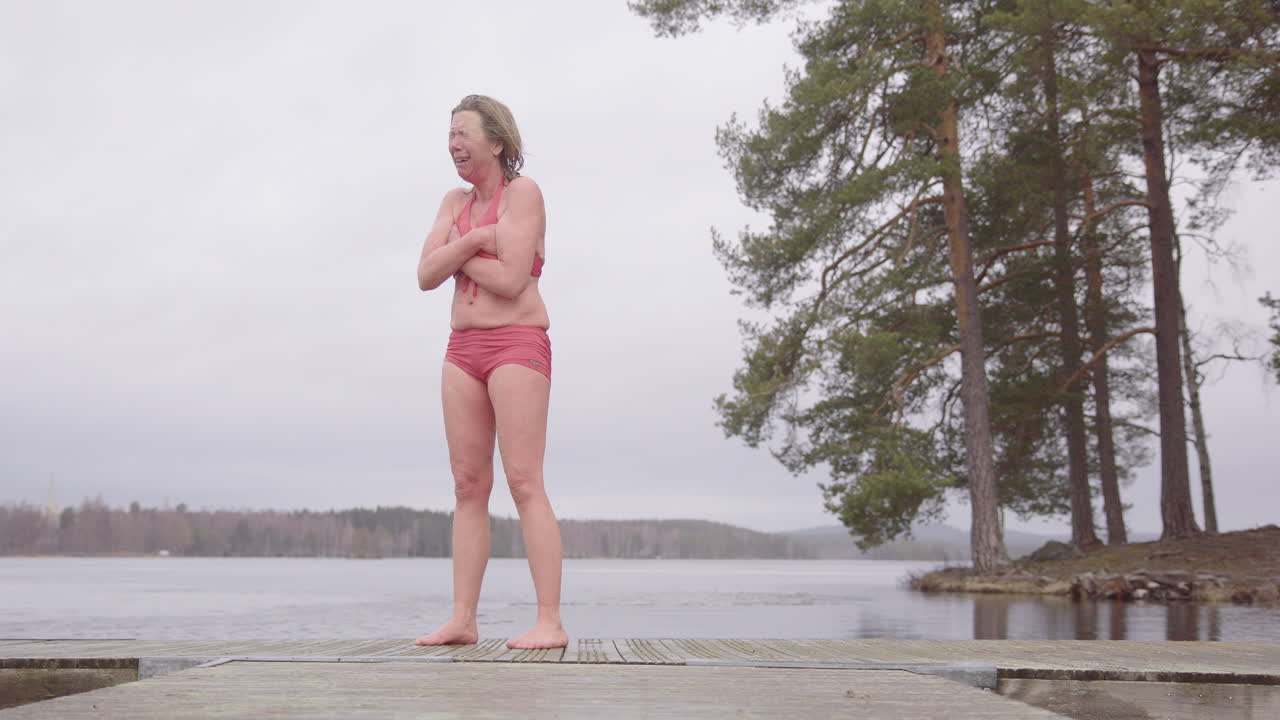 уязвимая женщина в комбинезоне плачет со сложенными руками после эмоционального погружения в ледяную воду.