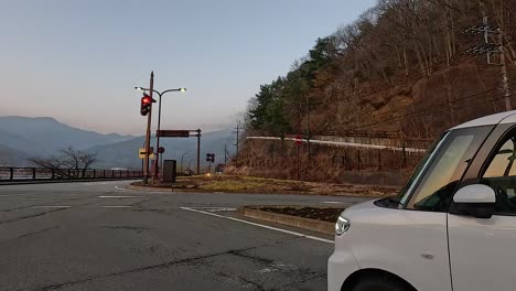 cars pass a traffic light on a mountain road in fujikawaguchiko, japan. the scene captures a serene evening with natural surroundings
