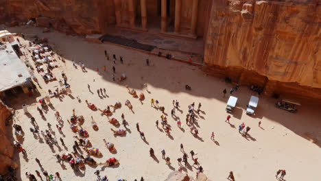 High-angle-pan-across-crowds,camels,-tourists,-and-vendors-outside-of-famous-Petra-stone-temple