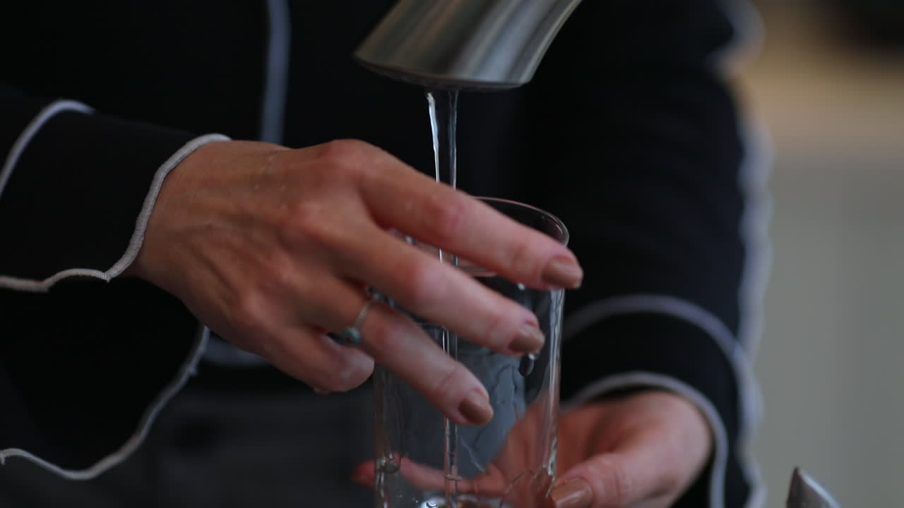 Adult woman rinses drinking glass with water from a sink faucet. Close up on hands.