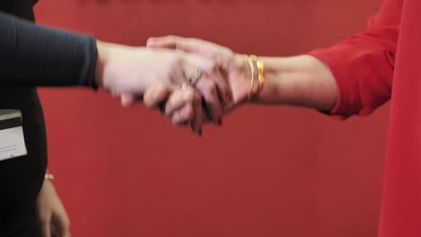 Elegant women greeting, perfect handshake against red background