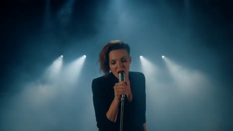female singer performing on stage with dramatic spotlights and smoke