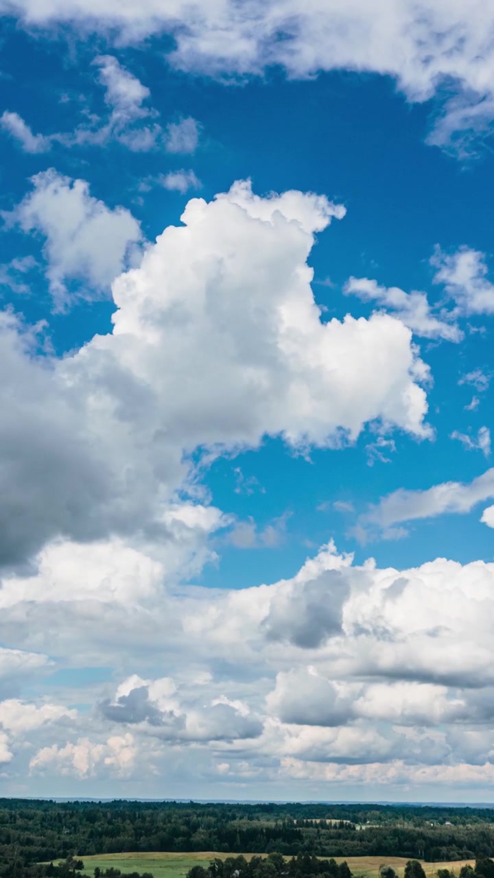 Vista hyperlapse verticale con drone di nuvole bianche e soffici che si muovono su un cielo azzurro brillante e un orizzonte di campagna verde e distante