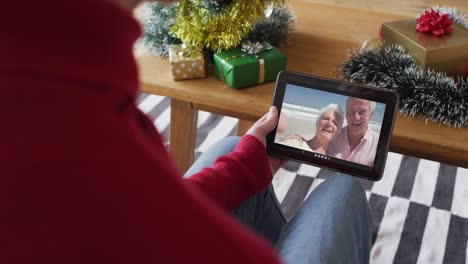 Caucasian-man-waving-and-using-tablet-for-christmas-video-call-with-smiling-couple-on-screen