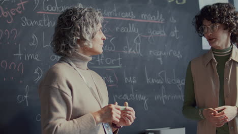 young female student and teacher talking at blackboard in english class