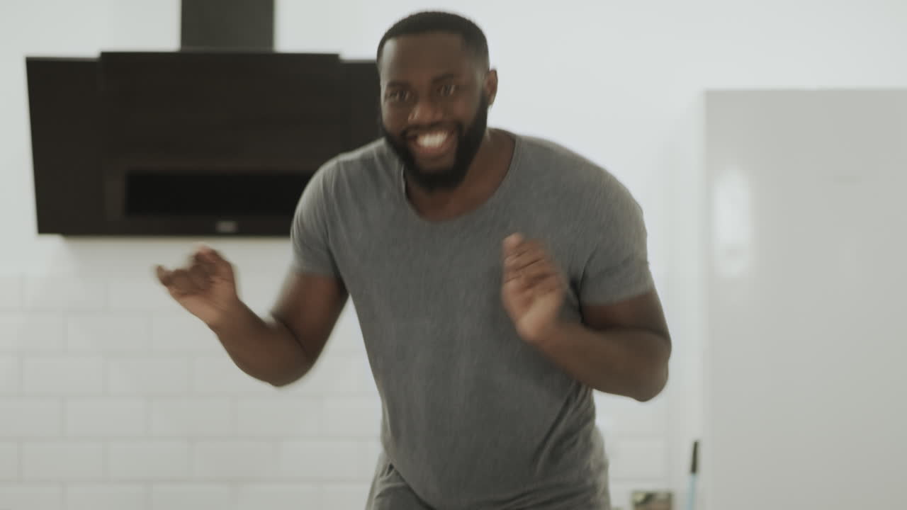 Happy black man dancing at open kitchen. Young guy making dance at home.