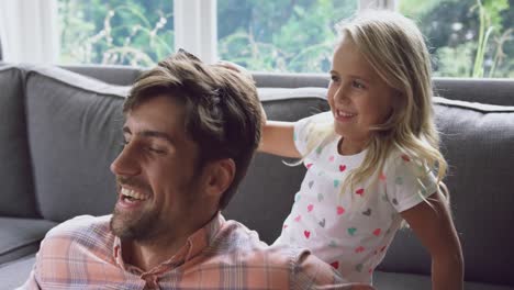 Young-daughter-combing-her-fathers-hair-on-sofa-at-home-4k