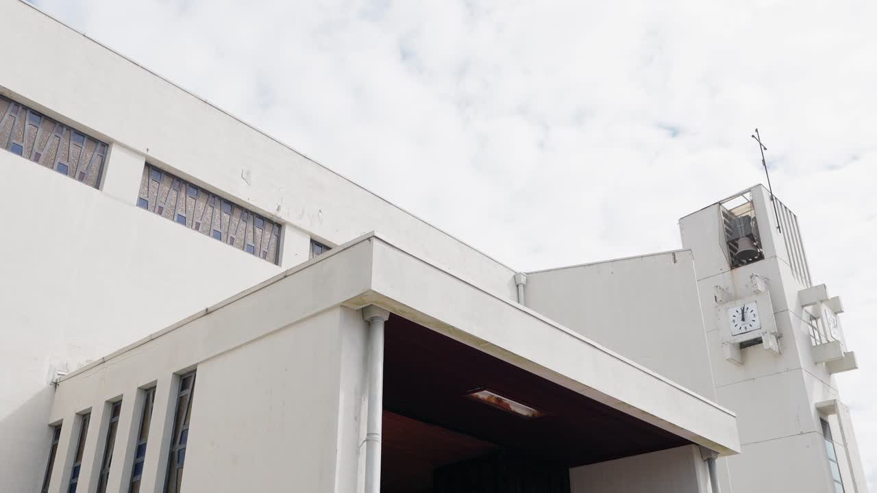 contemporary church building with clock and cross against overcast sky