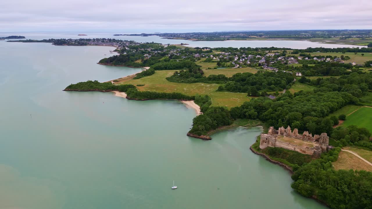 High-altitude drone slowly pulls back to reveal the Guildo Castle ruins, surrounding forest, sea, coastline and nearby towns in Brittany, France