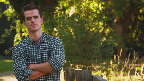 Portrait-Of-Casually-Dressed-Man-Leaning-On-Fence-On-Walk-In-Countryside