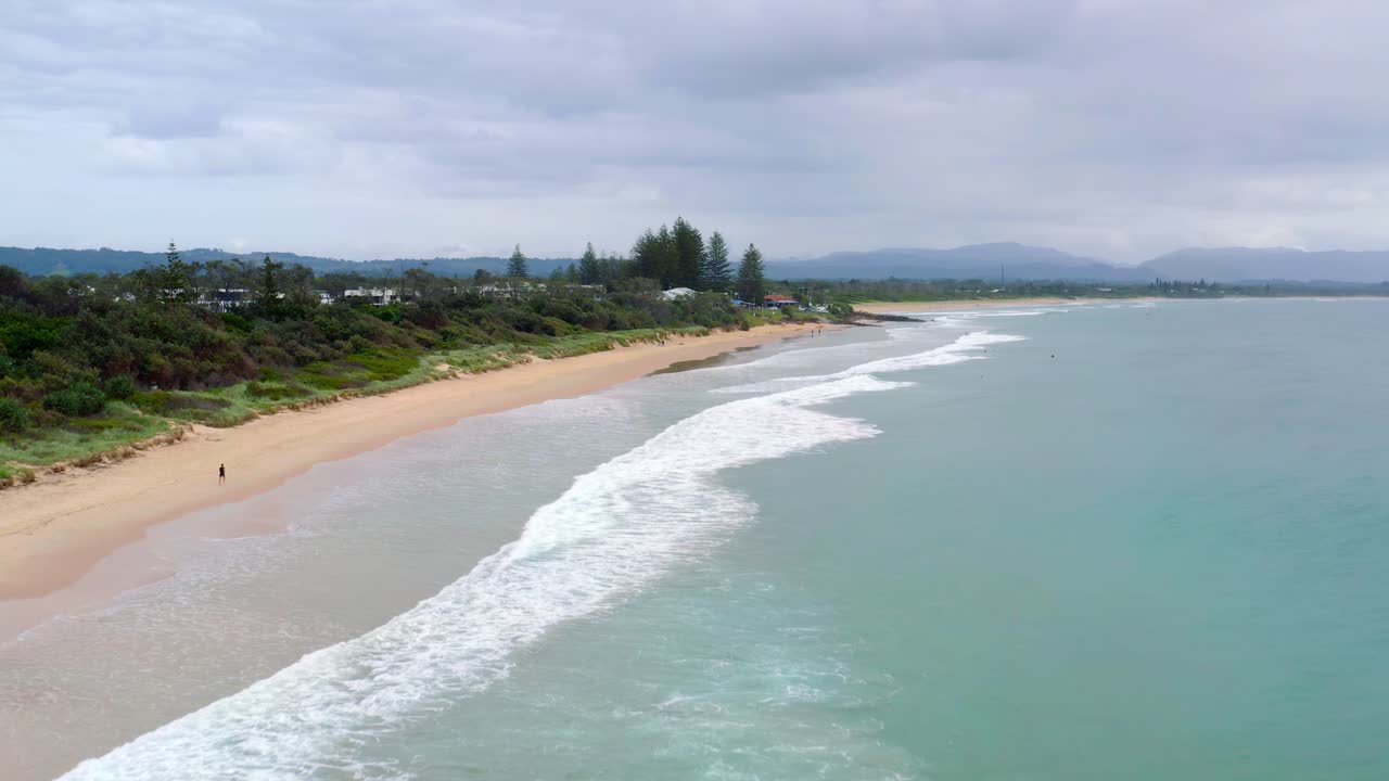 호주 바이런 베이(byron bay)의 모래 해변을 따라 달리는 관광객과 함께 해안선에 파도가 튀고 있습니다.