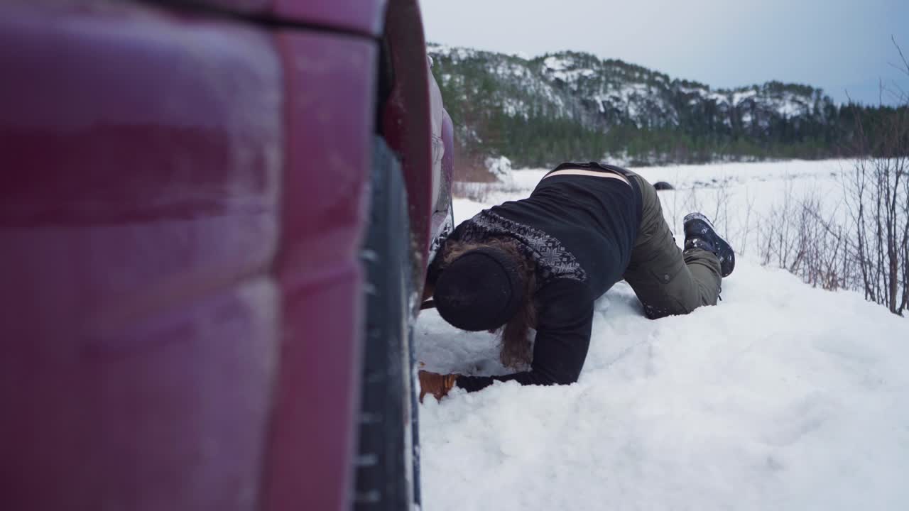 hombre noruego luchando para quitar la nieve debajo del vehículo se detuvo en terreno helado en invierno