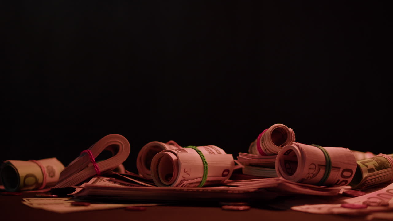 Piles of Rolled Cash and Banknotes on a Dark Table