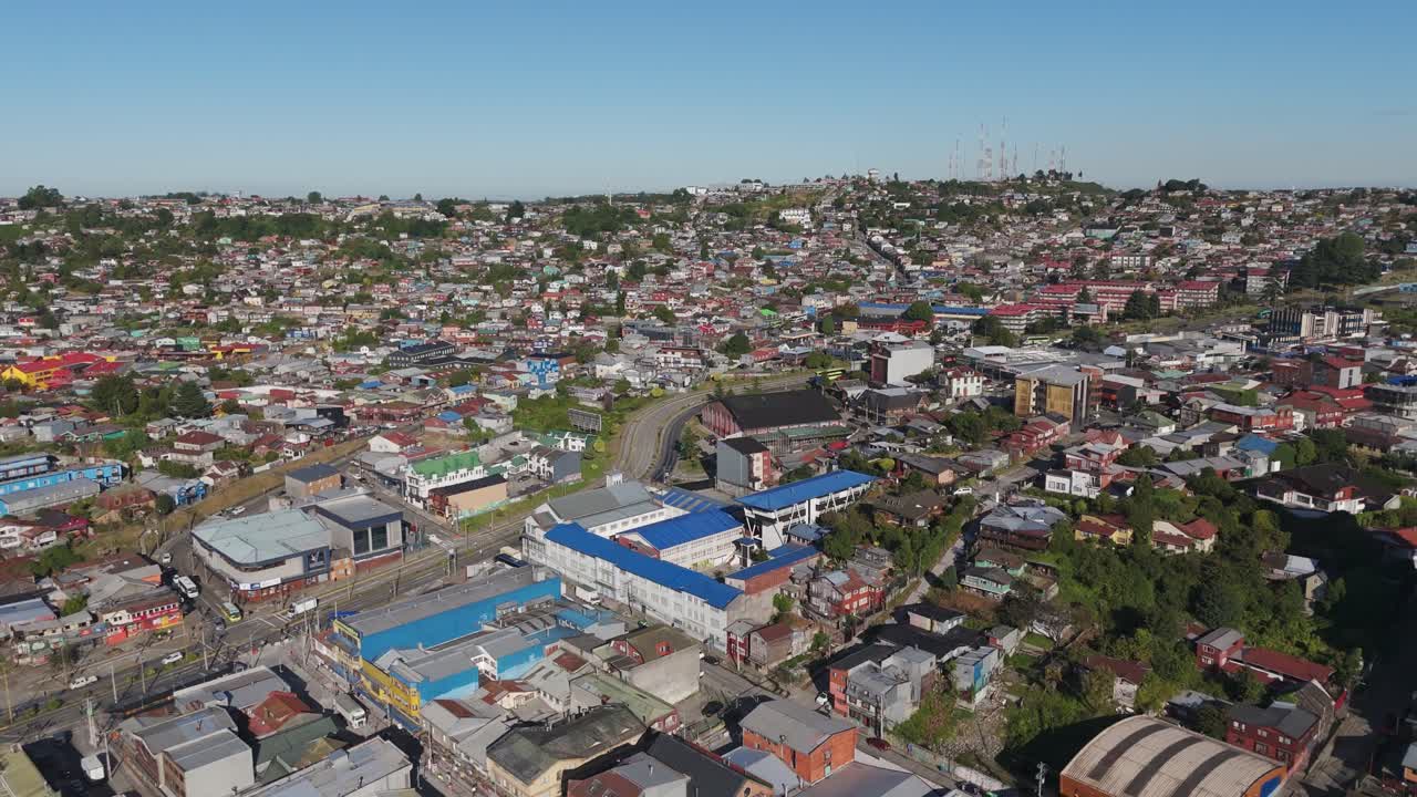 Aerial view of Puerto Montt cityscape, with colorful buildings and houses covering the hills under a clear sky, in Chile