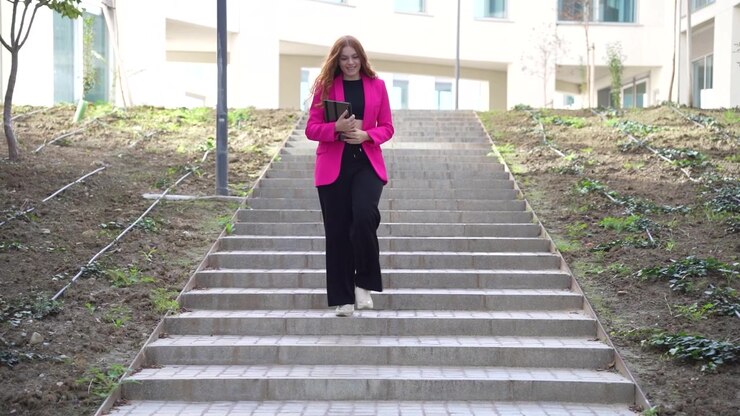 En elegant kvinde klædt i en stilfuld pink jakke stiger yndefuldt op ad havetrappen.