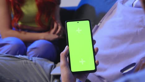 close up of woman with green screen mobile phone sitting on sofa at home with friends 1