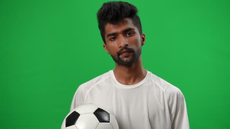 young perspiring middle eastern footballer wiping sweat off forehead sighing looking at camera. portrait of handsome tired sportsman posing at chromakey green screen. championship and sport concept.