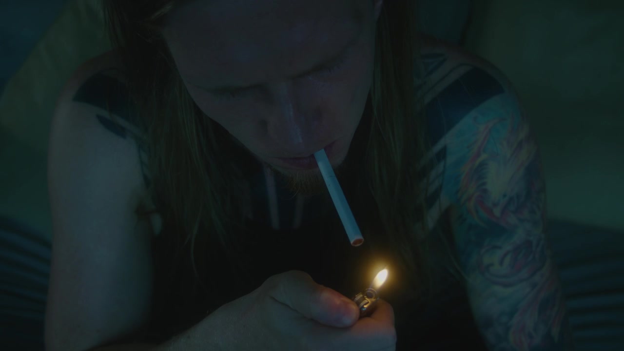 Young Man with Tattoos Lighting a Cigarette in Dim Light