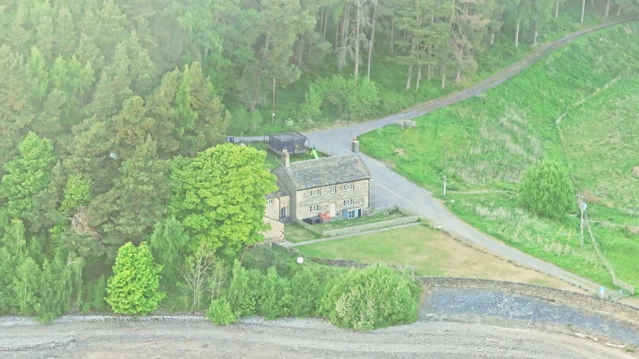 Aerial: house near Strines Reservoir, water storage reservoir, with forest during the day near Sheffield, South Yorkshire, England, crane down drone shot