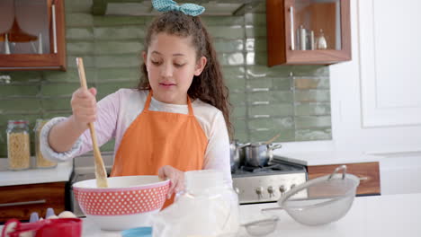 Feliz-Chica-Birracial-Con-Pelo-Largo-Y-Rizado-Mezclando-Masa-En-Un-Tazón-Y-Sonriendo-En-Una-Cocina-Soleada