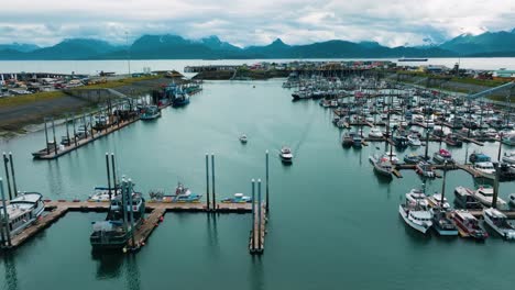 aerial drone pull away of halibut fishing boats pulling into marina and docking in small town homer alaska with beautiful mountain range backdrop