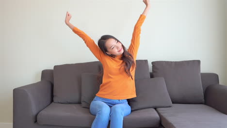 asian young woman in casual clothes stretching her arms over the head while sitting on a sofa daytime - static shot