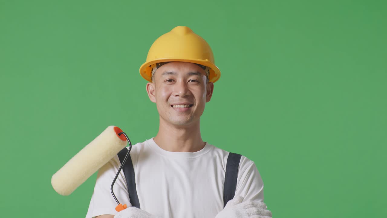Close Up Of Asian Man Painter Wearing Safety Helmet Smiling And Crossing His Arms While Standing In The Green Screen Background Studio