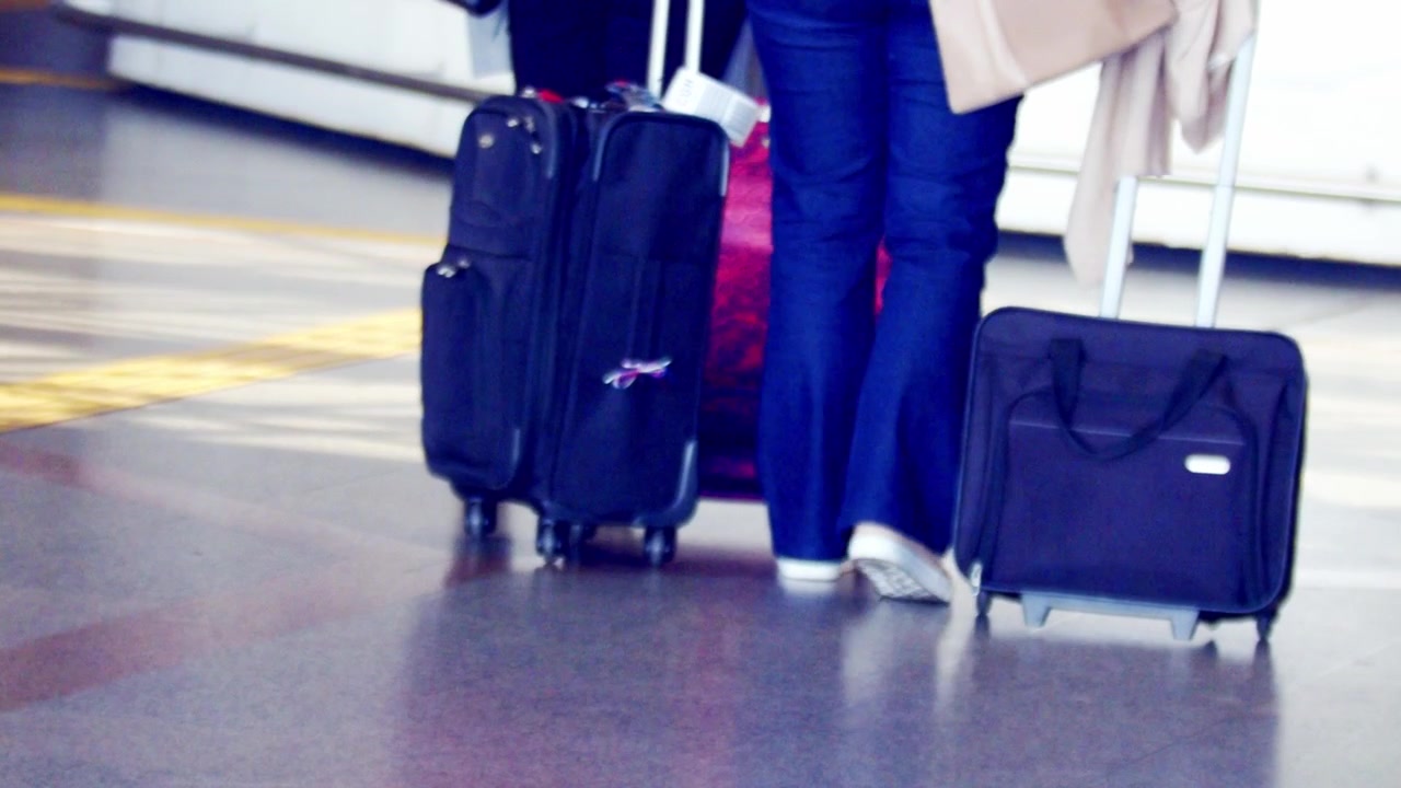 Super slow motion, faceless travellers rolling luggage while walking in airport