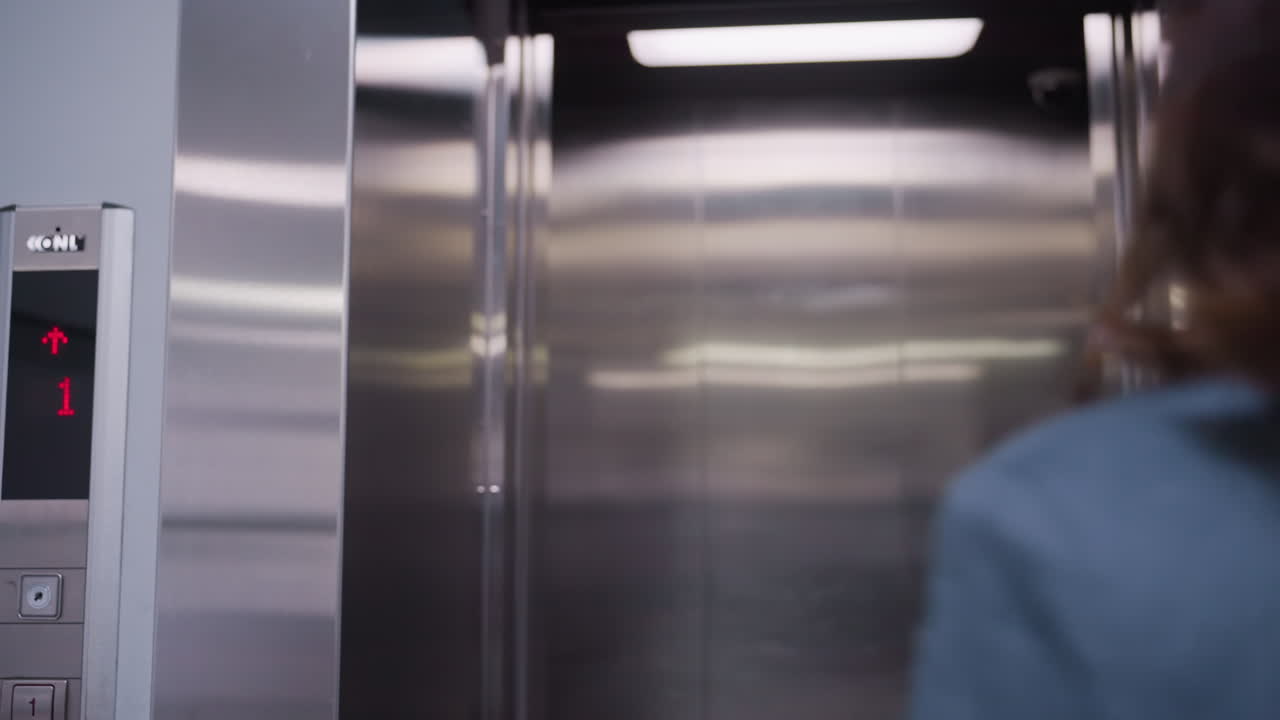 Businesswoman stepping out of elevator in modern office building. She smiles confidently, dressed in formal attire with a professional appearance. Corporate atmosphere in sleek, metallic elevator
