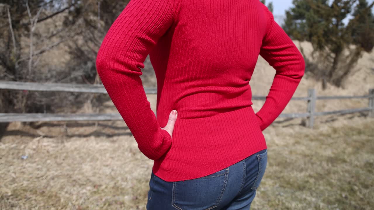 Woman in red top and jeans with hands on hips. Gimbal video moving around.