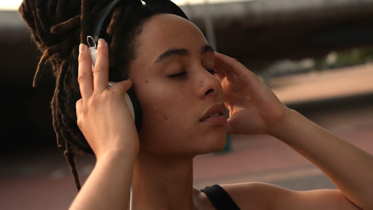 vista frontal de una joven mujer afroamericana escuchando música en auriculares en la ciudad 4k