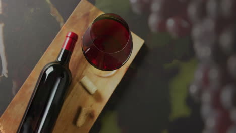 composite of red wine being poured into glass over wooden board on black background