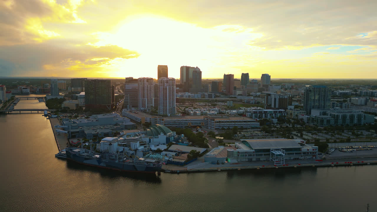 Establishing aerial pull back shot from above the Ybor city basin, showing the Tampa skyline and the bright sun filling the sky and sunlight casting a golden glow