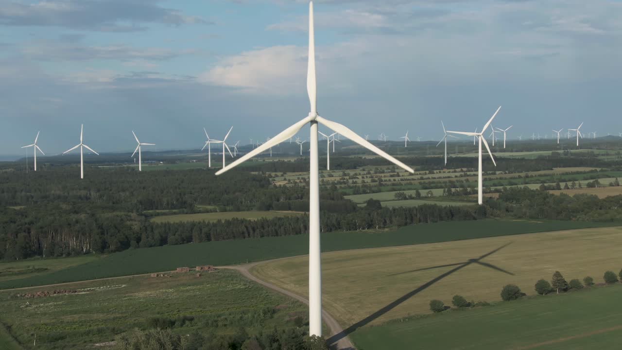 White Wind Turbines Harnessing Wind Energy On A Large Green Farm On A Sunny Day - Drone Shot (Pull-Back)