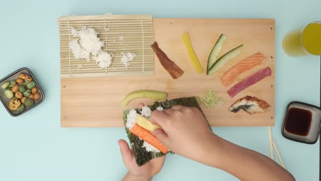 top shot of two hands preparing sushi on blue table