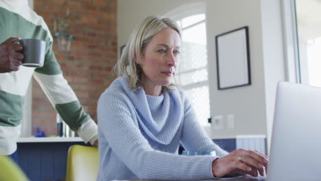 una pareja diversa estresada en la cocina sentada en la mesa, usando una computadora portátil