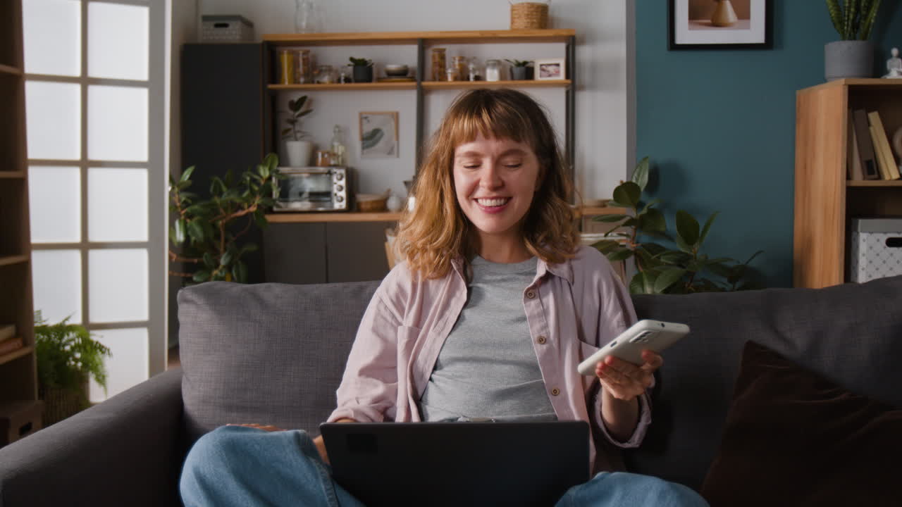 Woman sitting on couch with laptop and phone