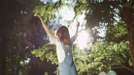 Young-Caucasian-cheerful-woman-in-glasses-spinning-around-with-hands-up-in-the-park-on-a-summer-day