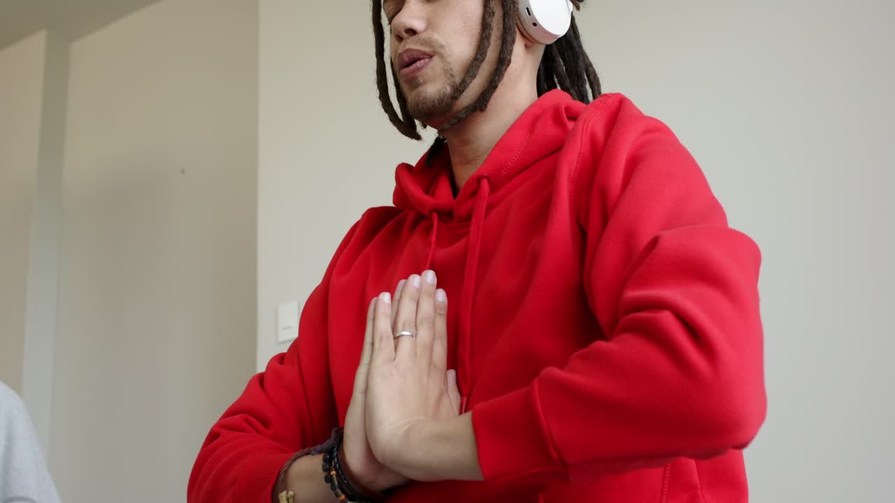 Depois de um homem de moletom e calças de abrigo usando fones de ouvido meditando em casa com pulseiras se alongando